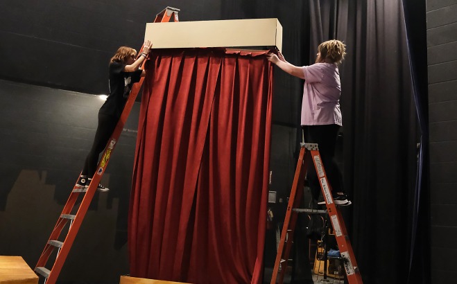 Students hanging curtains on piece of set on stage