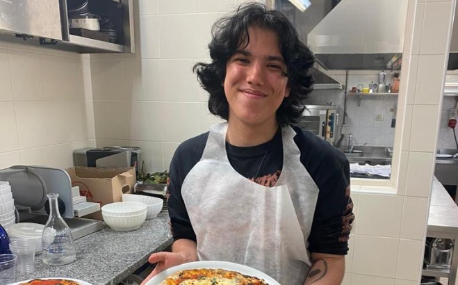 Kris holding a pizza he made in a kitchen in Italy