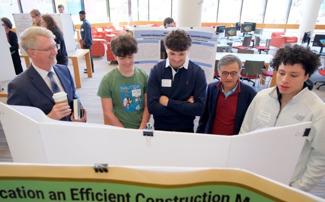Smiling faculty and students looking at presentation boards