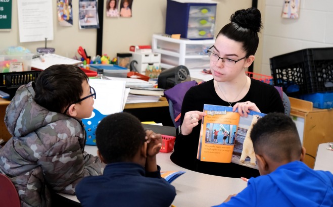 Female student teacher at table reading to students
