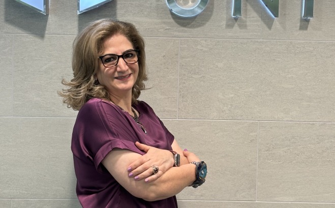 Mojdeh Bayat, Dean of Education in front of shield on the wall