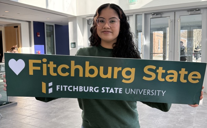 Adriana holding heart Fitchburg State sign in Antonucci lobby