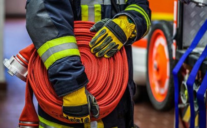 Closeup of firefighters hands holding a hose in front of truck