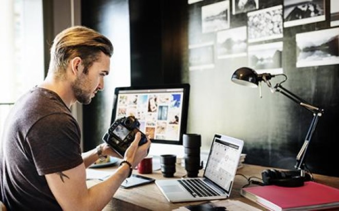 Male student at desk with camera and computers.
