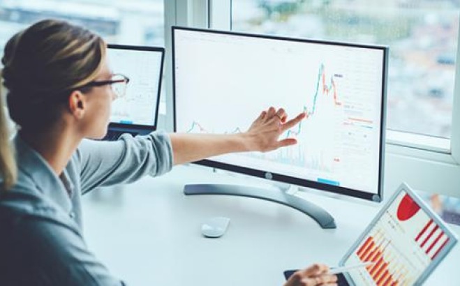 Women at desk pointing at line graph on computer screen.