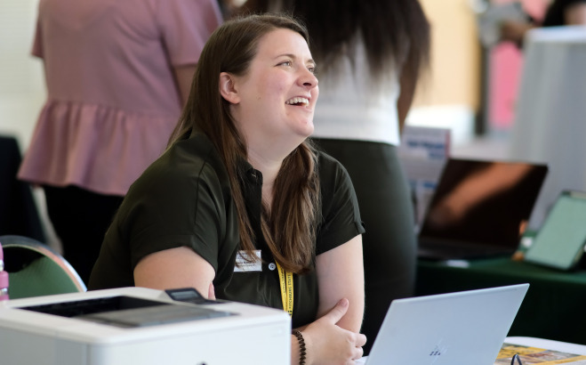 Staff member smiling with laptop at table in Hammond Main Lounge.