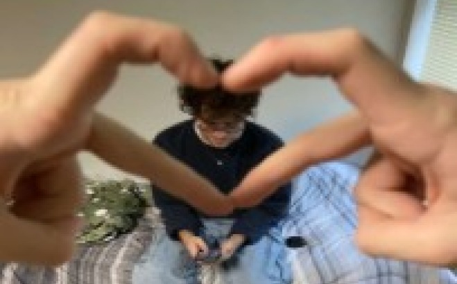 Zach Lamb ACT tutor on bed framed with heart fingers.
