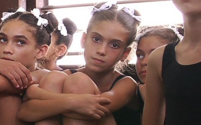 Ballet students sitting with arms around legs listening to instructor