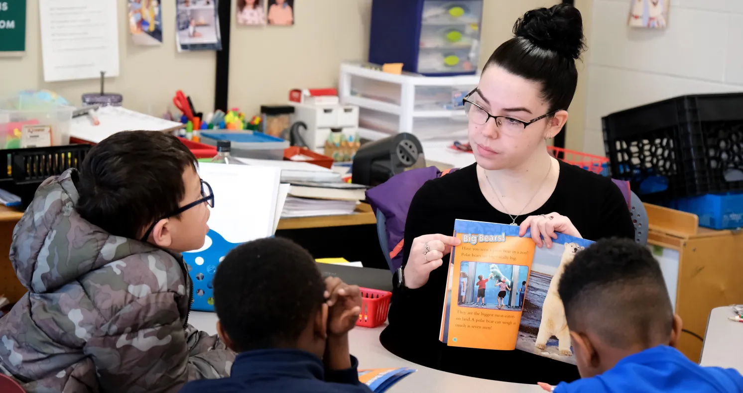 Female student teacher at table reading to students