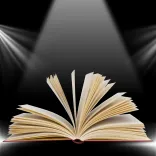 An open book with fanned-out pages under a spotlight against a dark background.