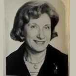 Black-and-white portrait of a woman with short, dark, wavy hair, a striped top, and dark blazer.