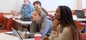 Two female students sitting in a classroom with others in the background