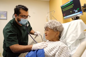 Male nursing student listening to heart of patient in hospital bed