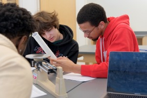 Three male students working with beaker and scale in earth systems science lab