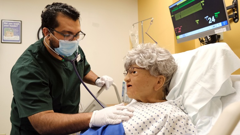 Male nursing student listening to heart of patient in hospital bed