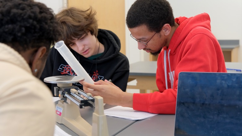 Three male students working with beaker and scale in earth systems science lab