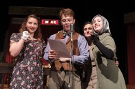 One male and three female actors performing in front of the microphone on stage