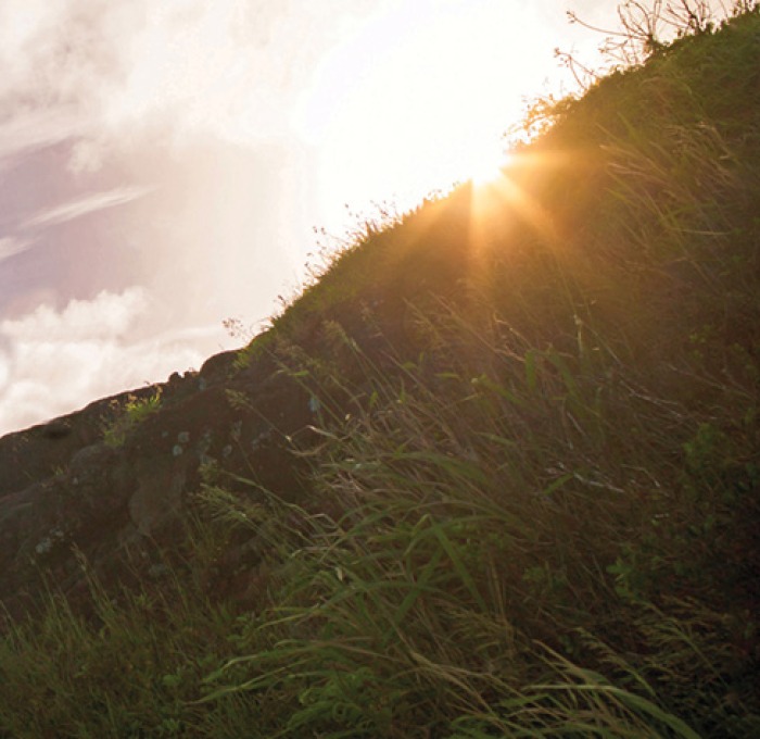 Picture of green hillside with the sky, clouds and sun