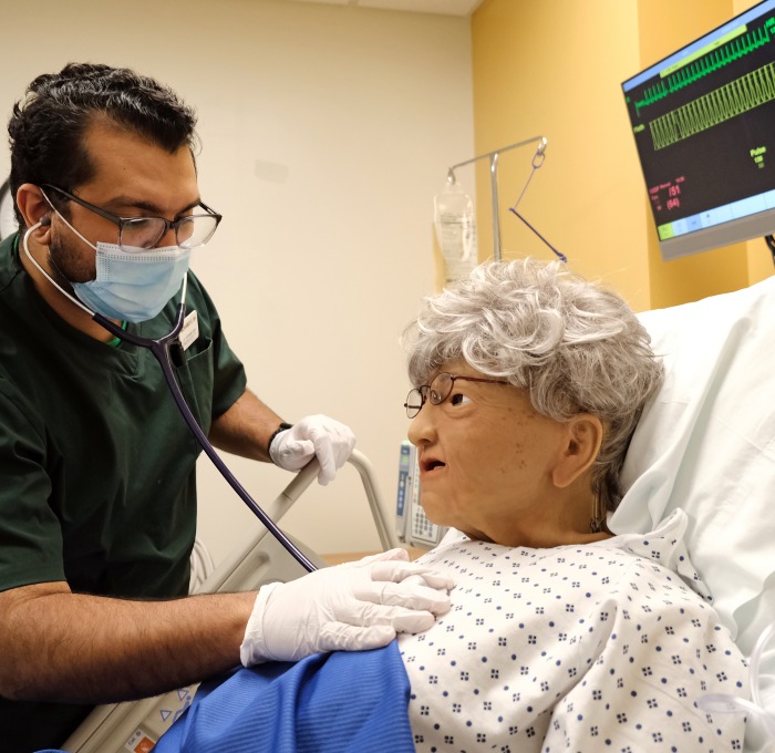Male nursing student listening to heart of patient in hospital bed