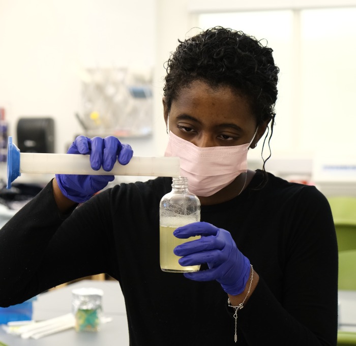 Female student pouring chemicals into a beaker in chemistry lab