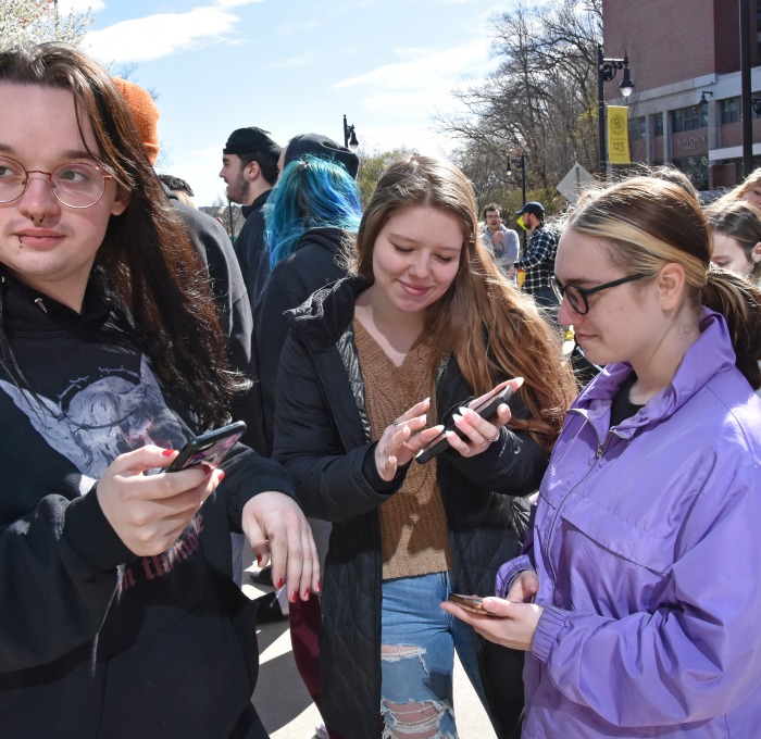 Three students on their phones in front of Hammond Hall with Aubuchon Hall in background