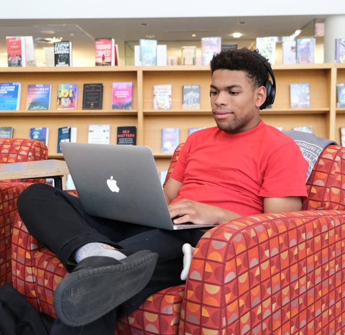 Male student sitting in chair on his laptop in the library