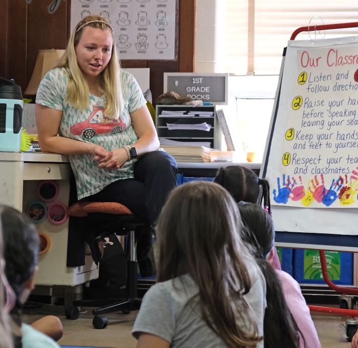 teacher sitting in front of a classroom talking to students