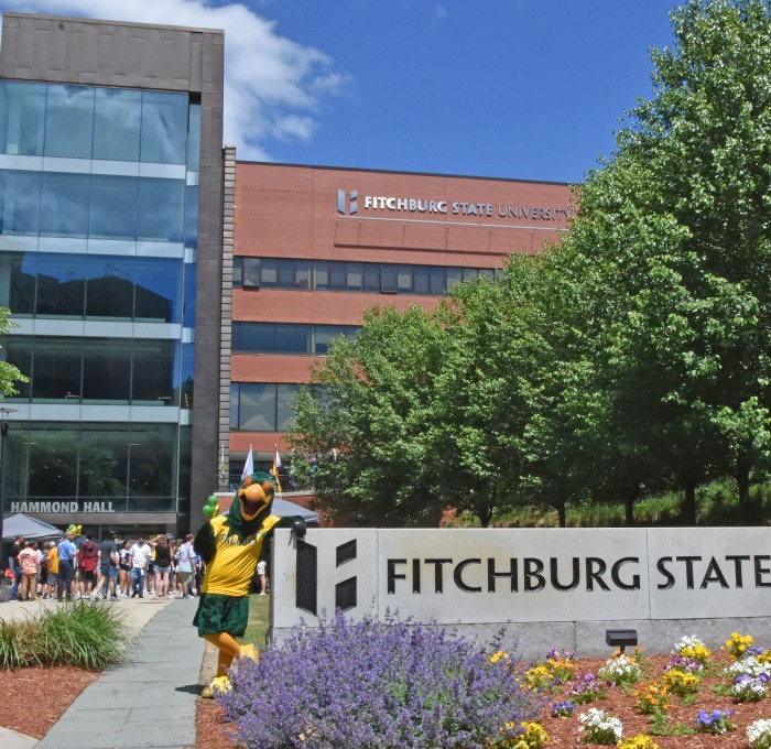 Freddy with sign in front of Hammond Hall with students in background