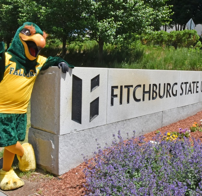Freddy standing next to Fitchburg State University sign with flowers