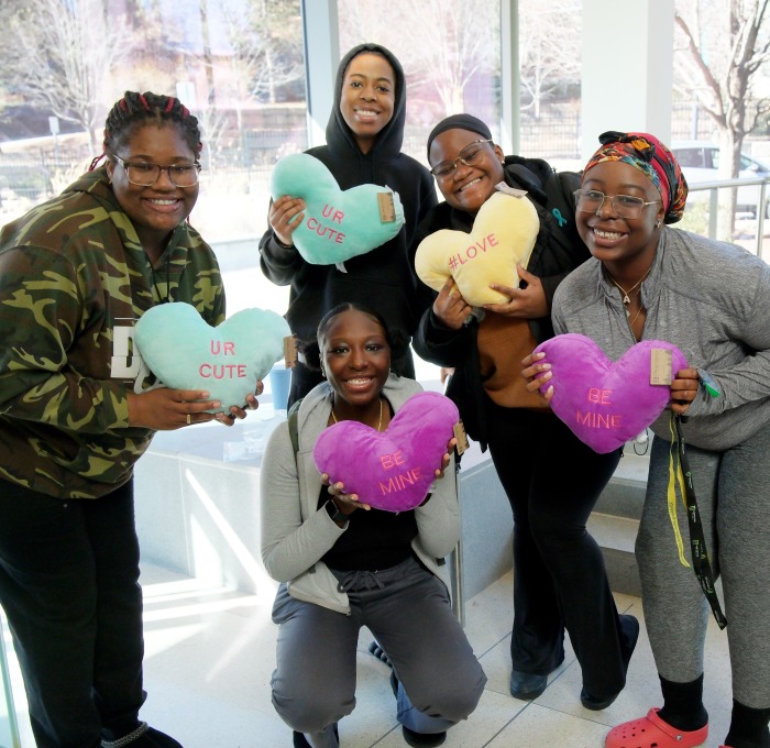 Female students showing off their stuffed heart pillows in Hammond street level