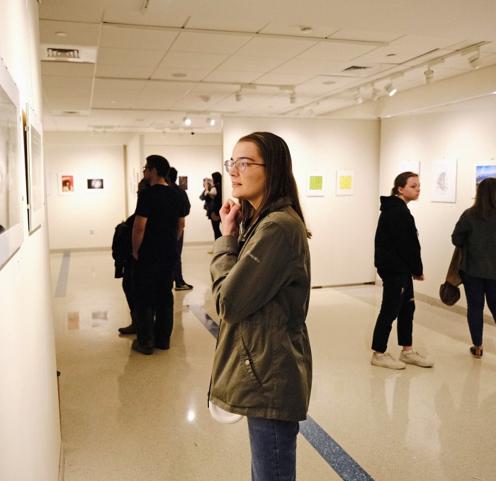 Photos on walls with students looking at them in gallery