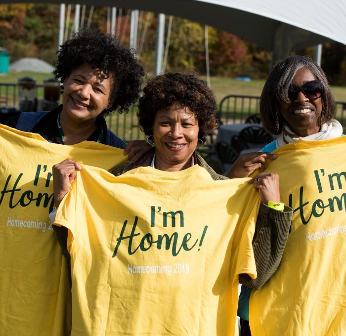 Three female alum at homecoming in end zone holding I'm Home t-shirts