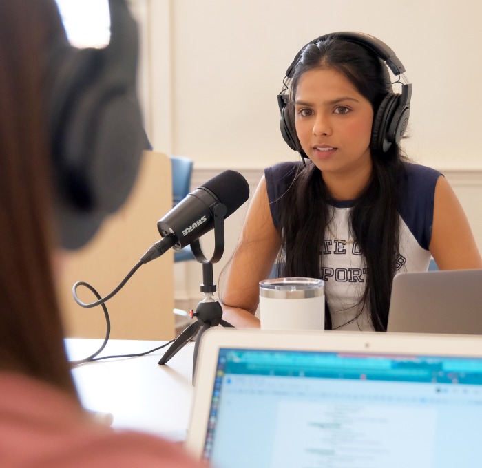 Two female students with headphones, microphones, and laptops doing podcast