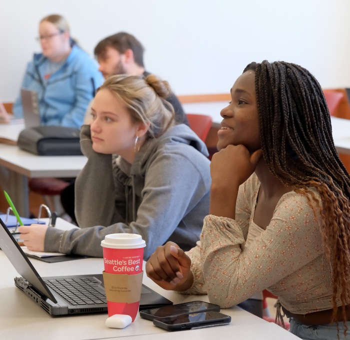 Two female students sitting in a classroom with others in the background