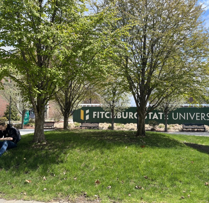 Student sitting on highland plaza near gazebo in front of mailboxes and mail center