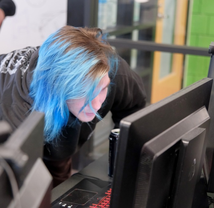 Student with blue hair on desktop computer in classroom