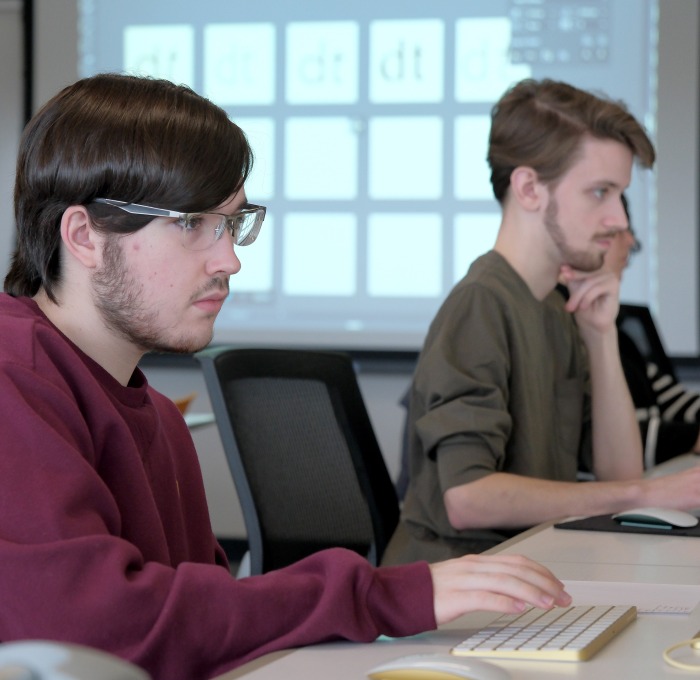 Two male students on computers in communication classroom