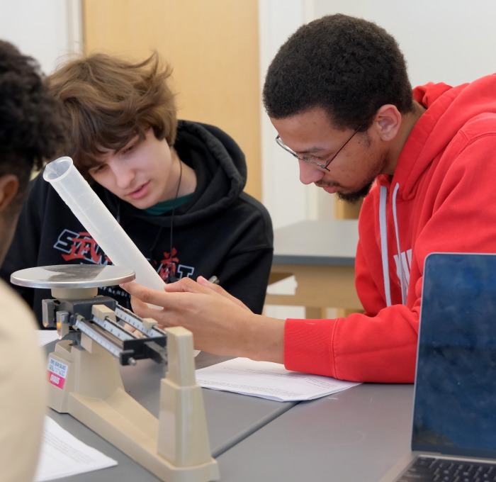Three male students working with beaker and scale in earth systems science lab