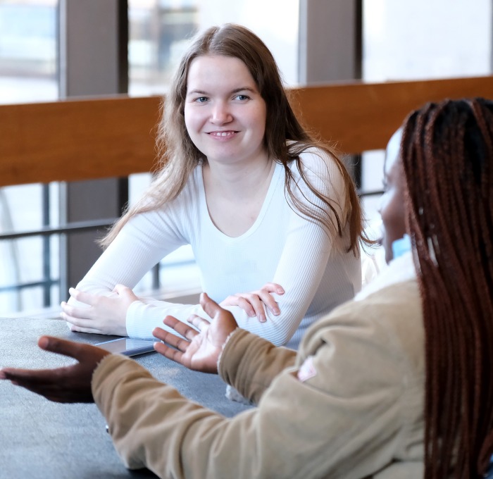 Smiling female students in the main lounge sitting at a table. 