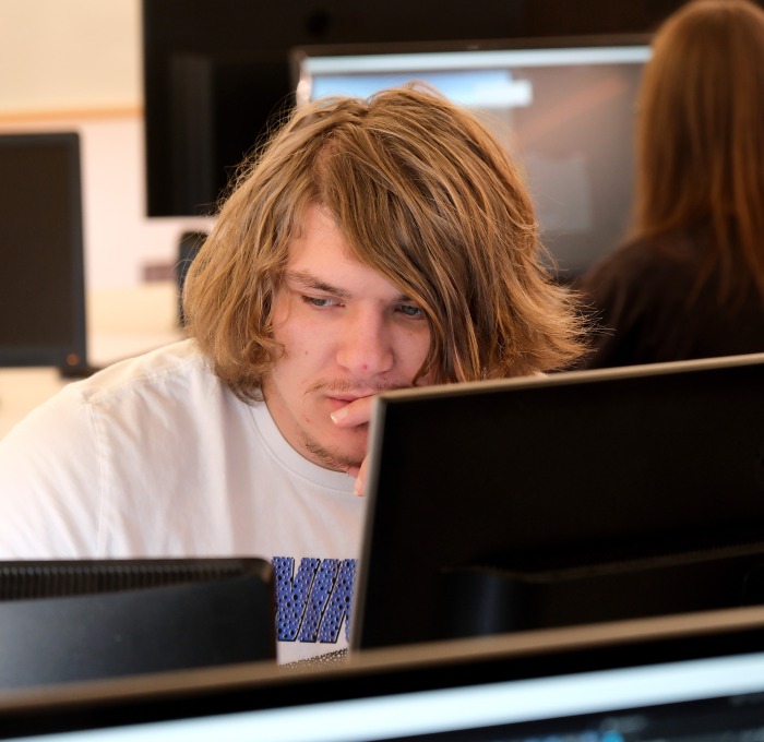 Male student behind computer screens and another student in background