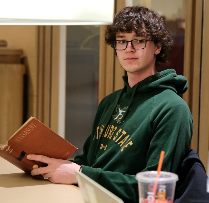 Male student sitting at table with lamp reading book in archives