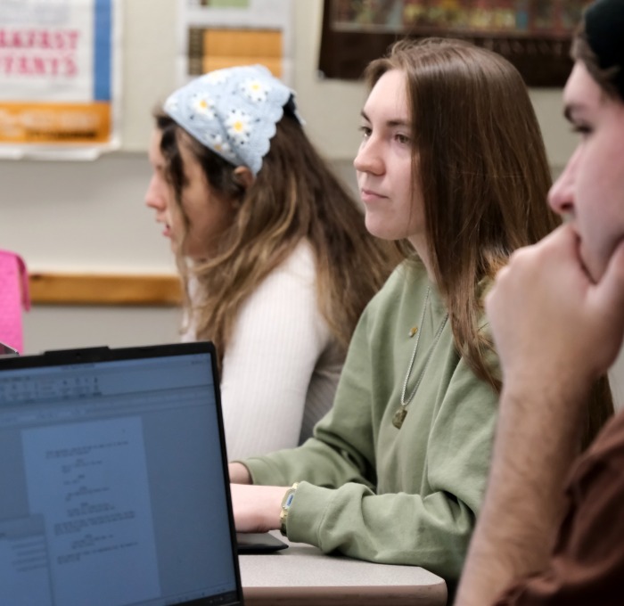 Two female and one male student behind laptops in class