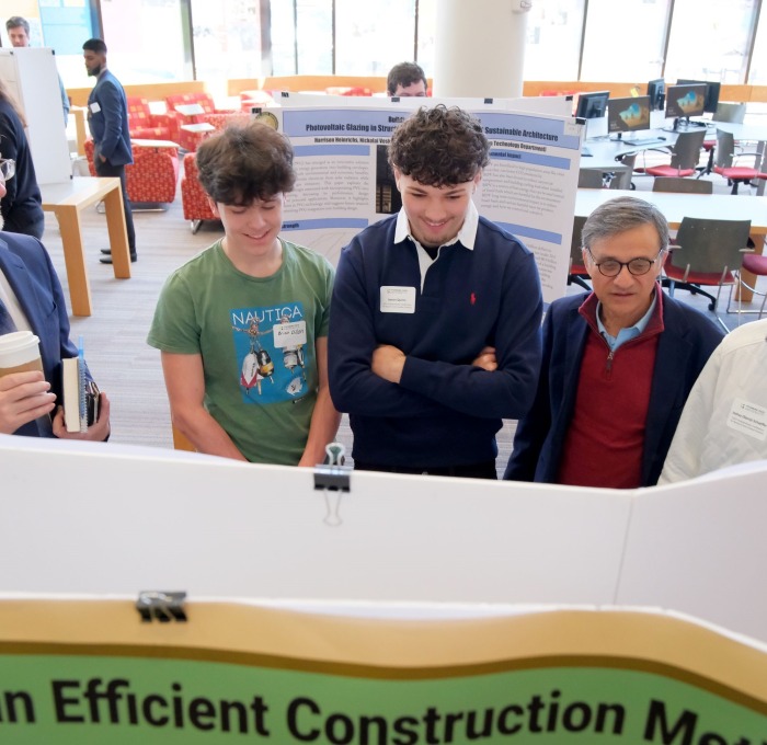 Smiling faculty and students looking at presentation boards