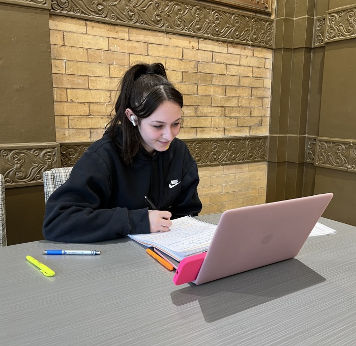 Female student with laptop, notebook, pens and highlighters in Thompson lobby
