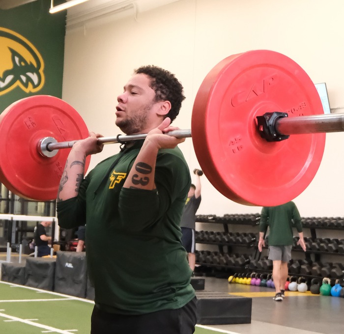 Student lifting a barbell in gym at landry