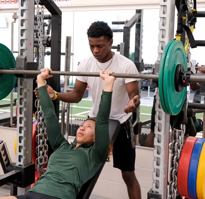 Student bench pressing with a spotter in gym at landry