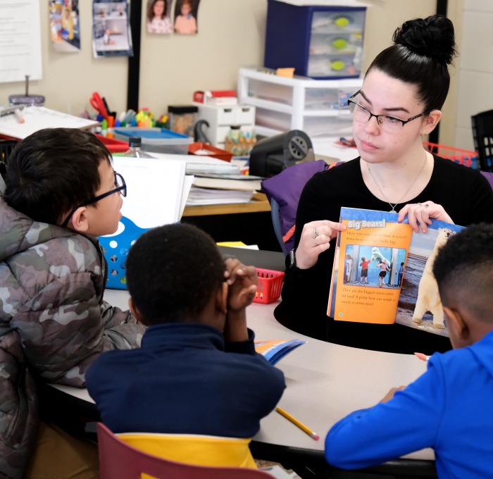 Female student teacher at table reading to students