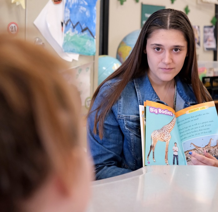 brunette student teacher at table with book in the classroom