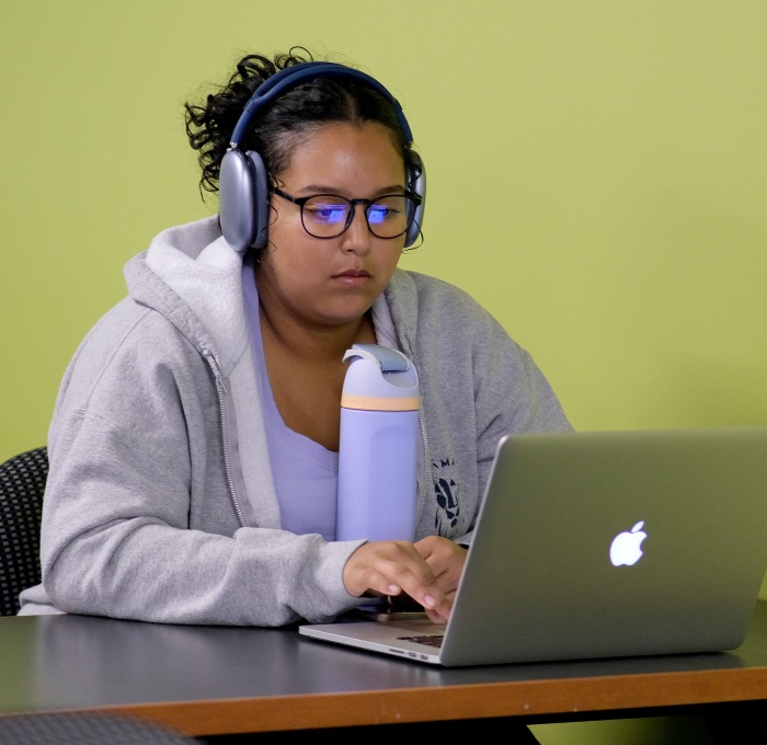 Student on laptop with headphones and water bottle at table in room