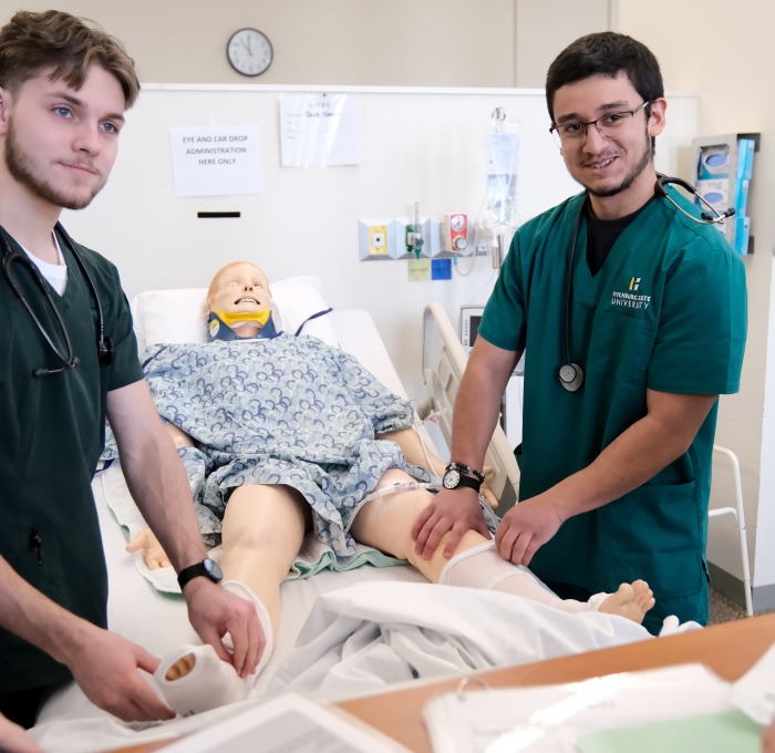 Two male nurses working on mannequin in the bed in lab